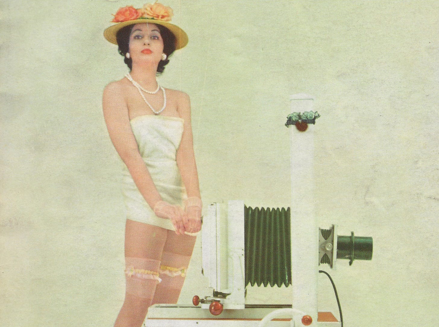 woman model wearing flowery hat and silk stockings. there is a large format camera beside her. 