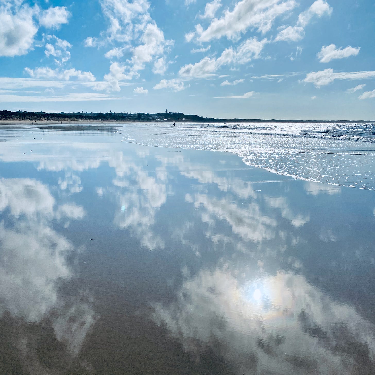Ocean Grove beach: wide angle; blue sky and clouds reflected in the shallow water, surf to the right; tiny figures in the distance