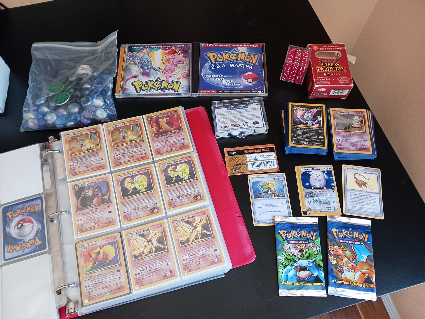 More items from Ryan’s collection, including a WotC ID card, misprinted TCG Base set booster packs, music albums, TCG counters and coins, and fake cards