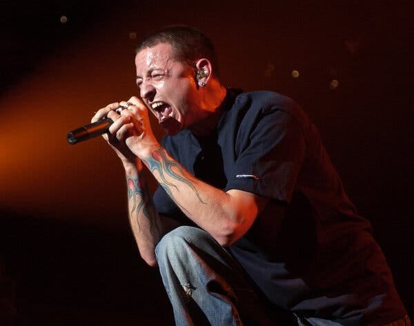 Chester Bennington closes his eyes and screams, one leg propped up on a monitor and his hands grasping the microphone close to his mouth.