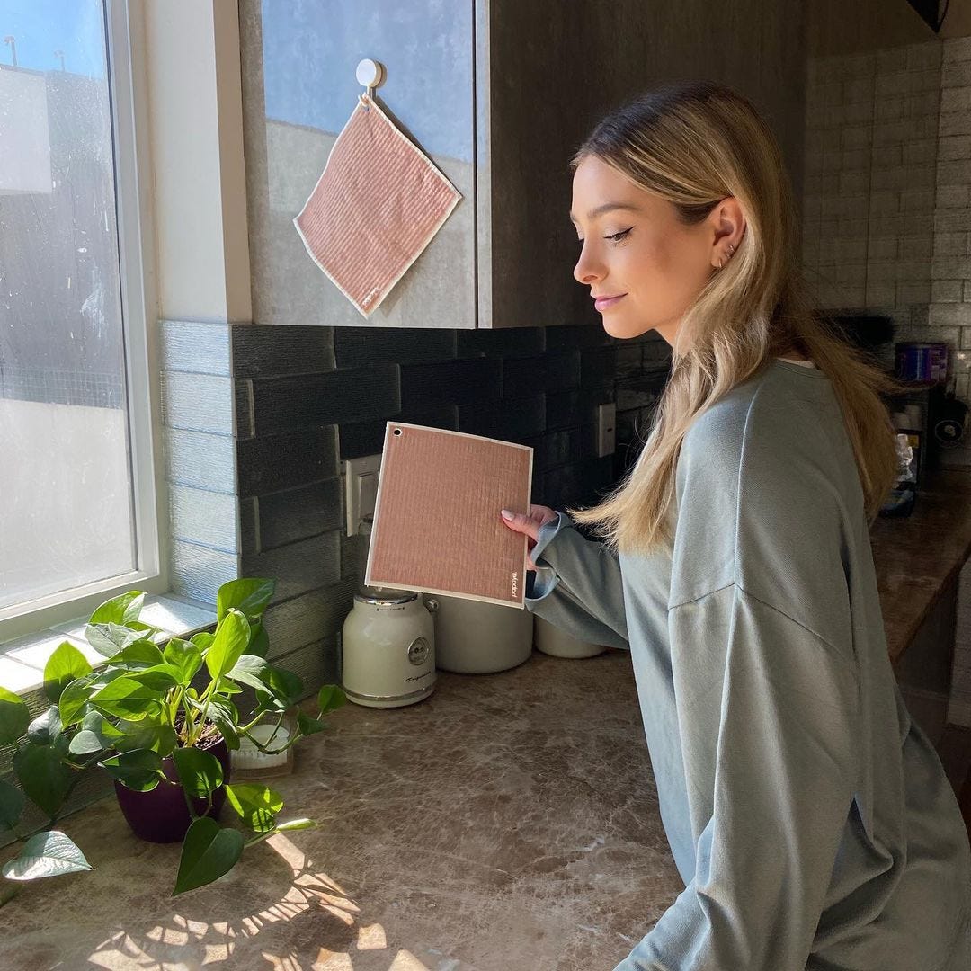 a model holding a cloth by a sink and another of the cloths hanging from a hook mounted on a cabinant