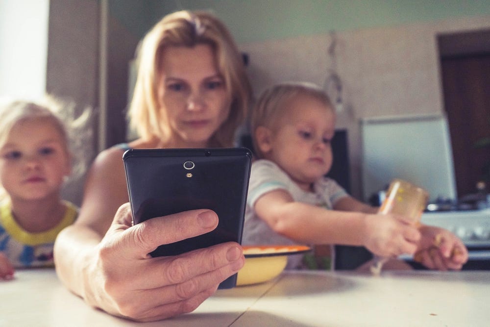 Mother looking at phone with two children, sitting at the table.