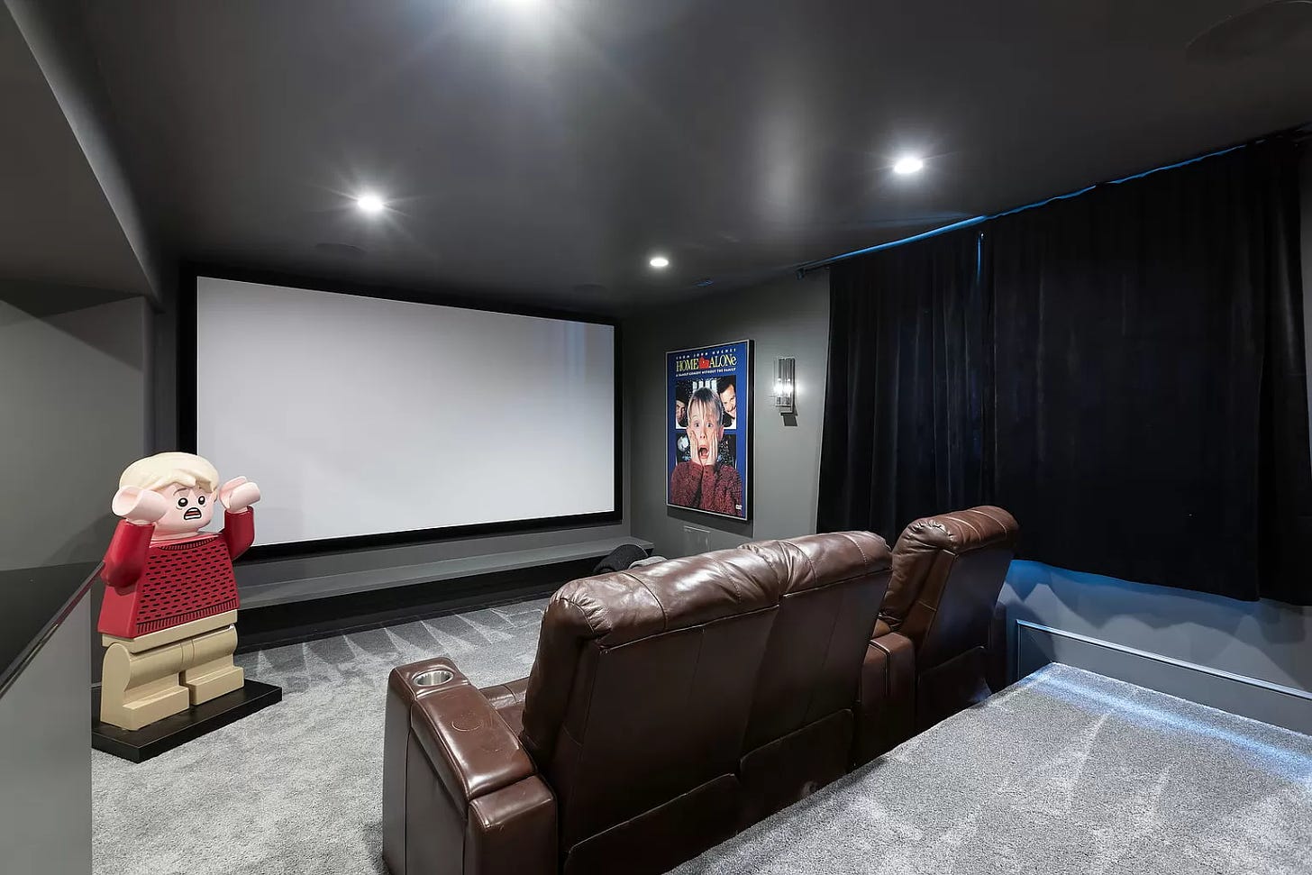 Dark gray movie room with a projector screen. There's a Home Alone poster in the corner and a giant Lego Kevin McAllister.