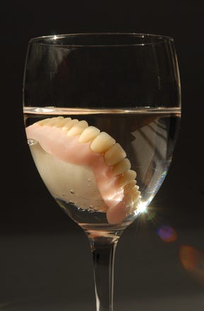 Dentures in a glass of water on black background.
