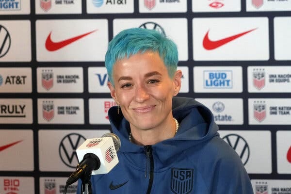 Megan Rapinoe smiling and sitting in front of a microphone during a news conference.