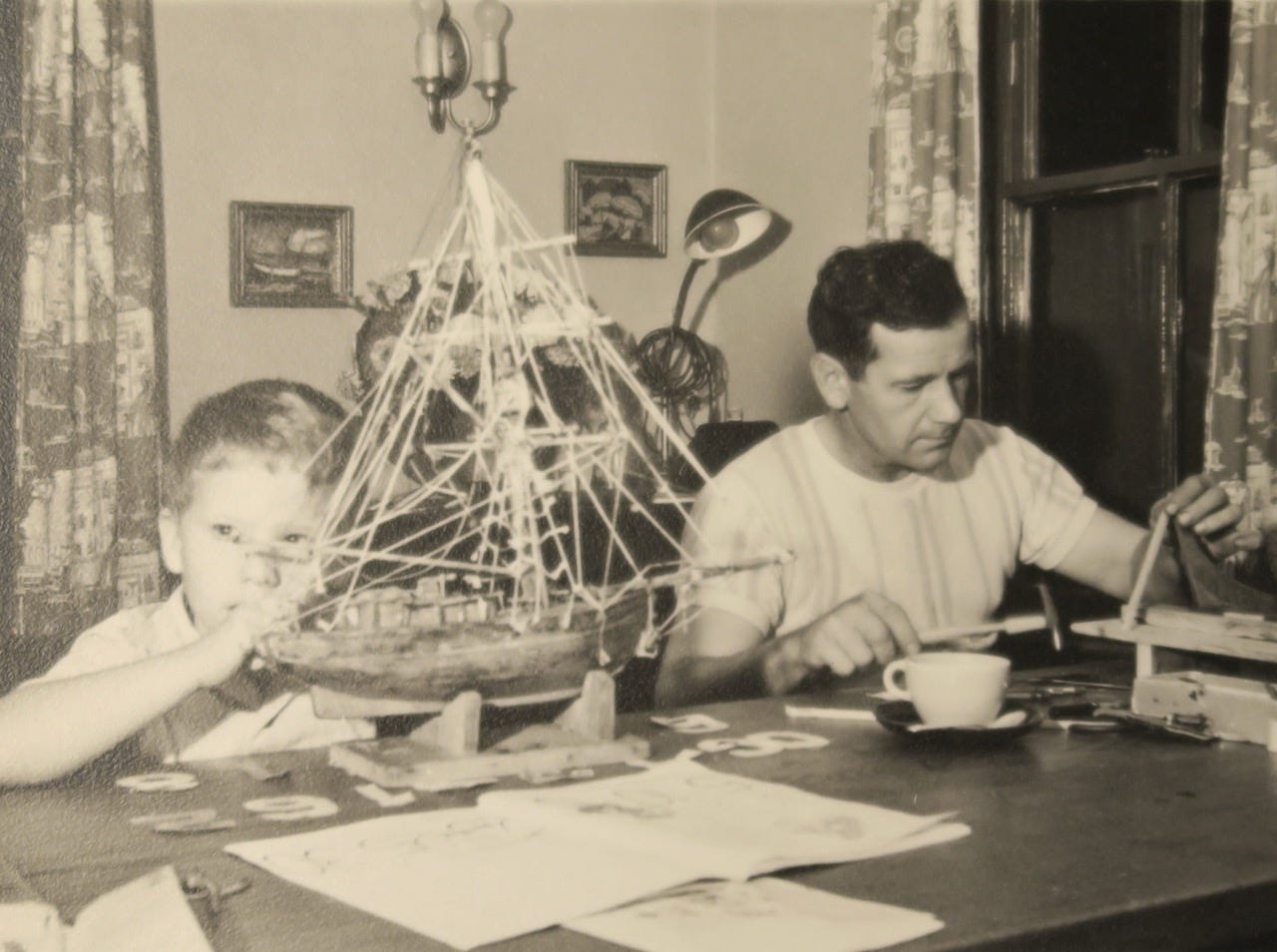 A person and a child sitting at a table with a model ship

Description automatically generated