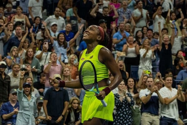 The tennis player Coco Gauff, in a neon green tennis top and skirt, smiles and looks upward.