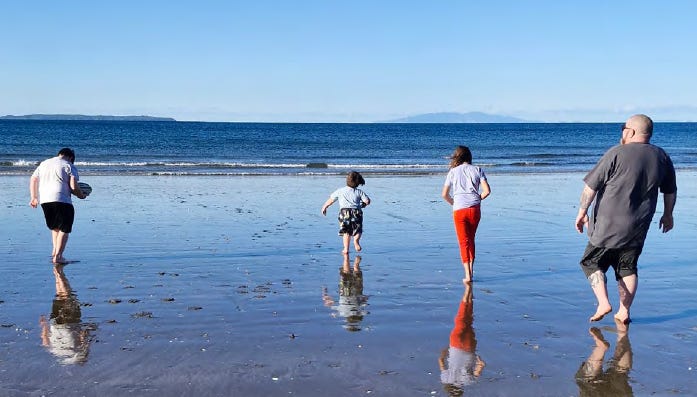 a parent and three kids walking towards the water at an auckland beach