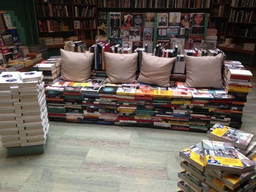 A big pile of books formed into the shape of a couch with 4 pillows on it. It seems like it's in a bookstore