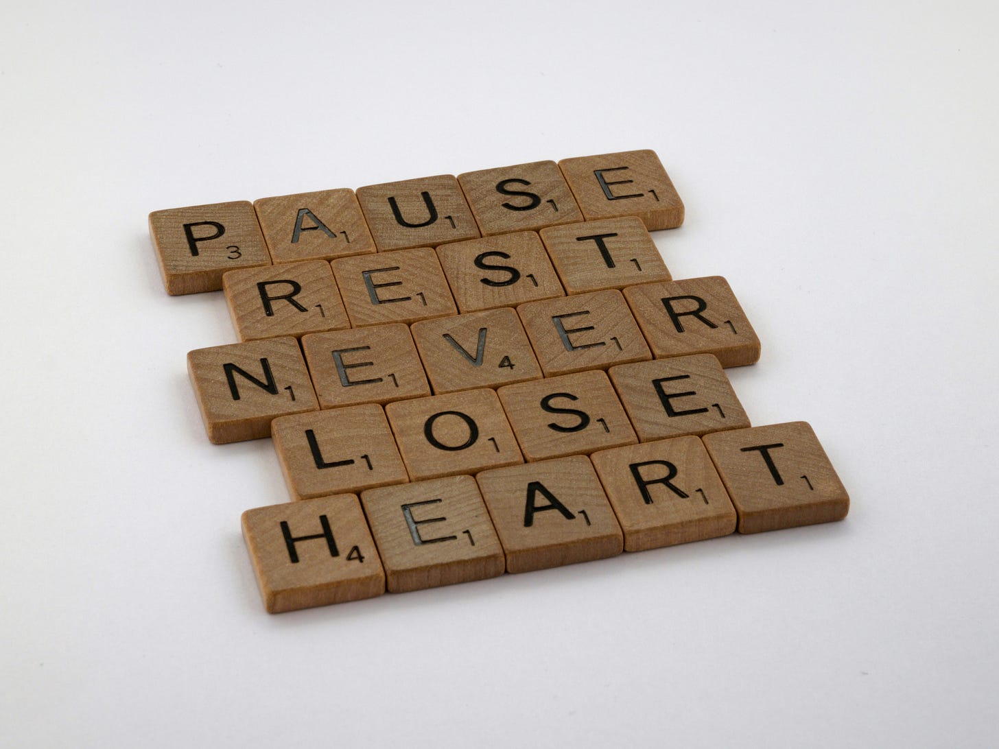 Scrabble tiles arranged to say "Pause, rest, never lose heart". The background is white