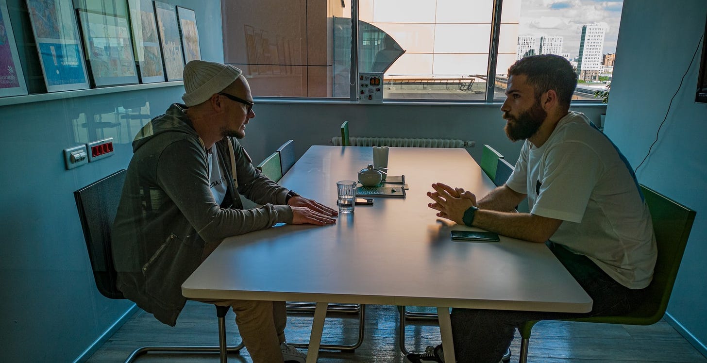 Two men speaking to each other over a table.