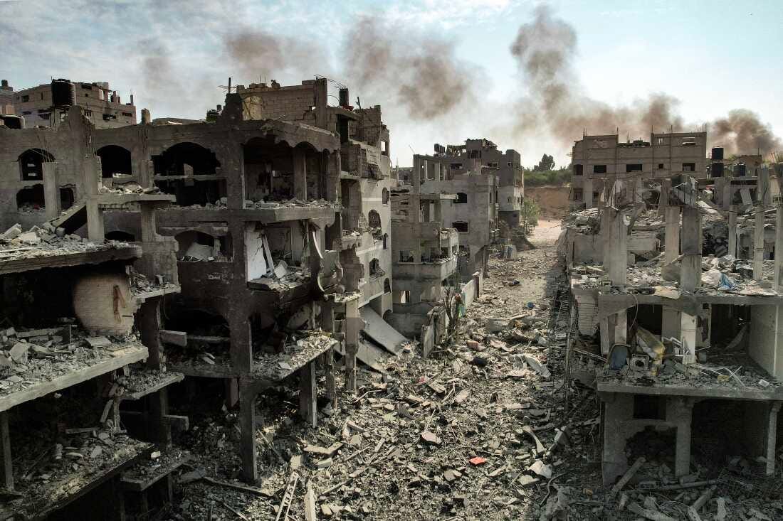 This photo shows buildings destroyed by Israeli airstrikes in Gaza's Jabalia camp for Palestinian refugees on Oct. 11, 2023. The skeletons of multistory buildings have rooms filled with rubble. The buildings stand along a road that is also filled with rubble.