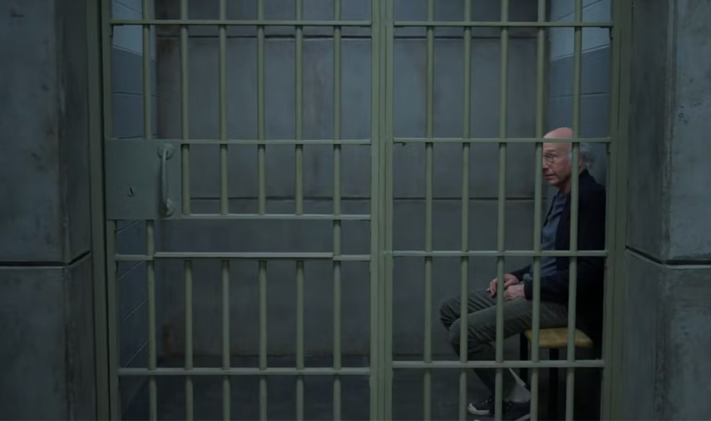 A screenshot from the Curb Your Enthusiasm finale of Larry David sitting in a jail cell