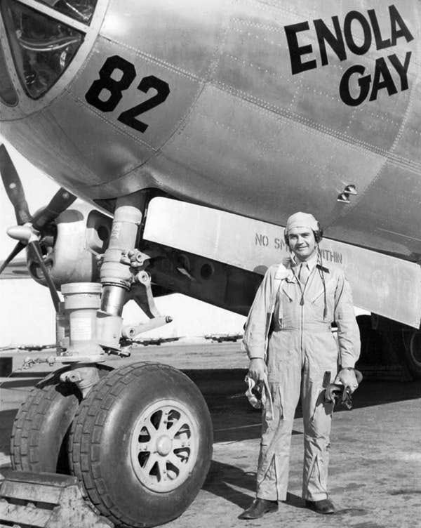 A person in a flight suit stands beside an aircraft named &quot;Enola Gay,&quot; with visible landing gear