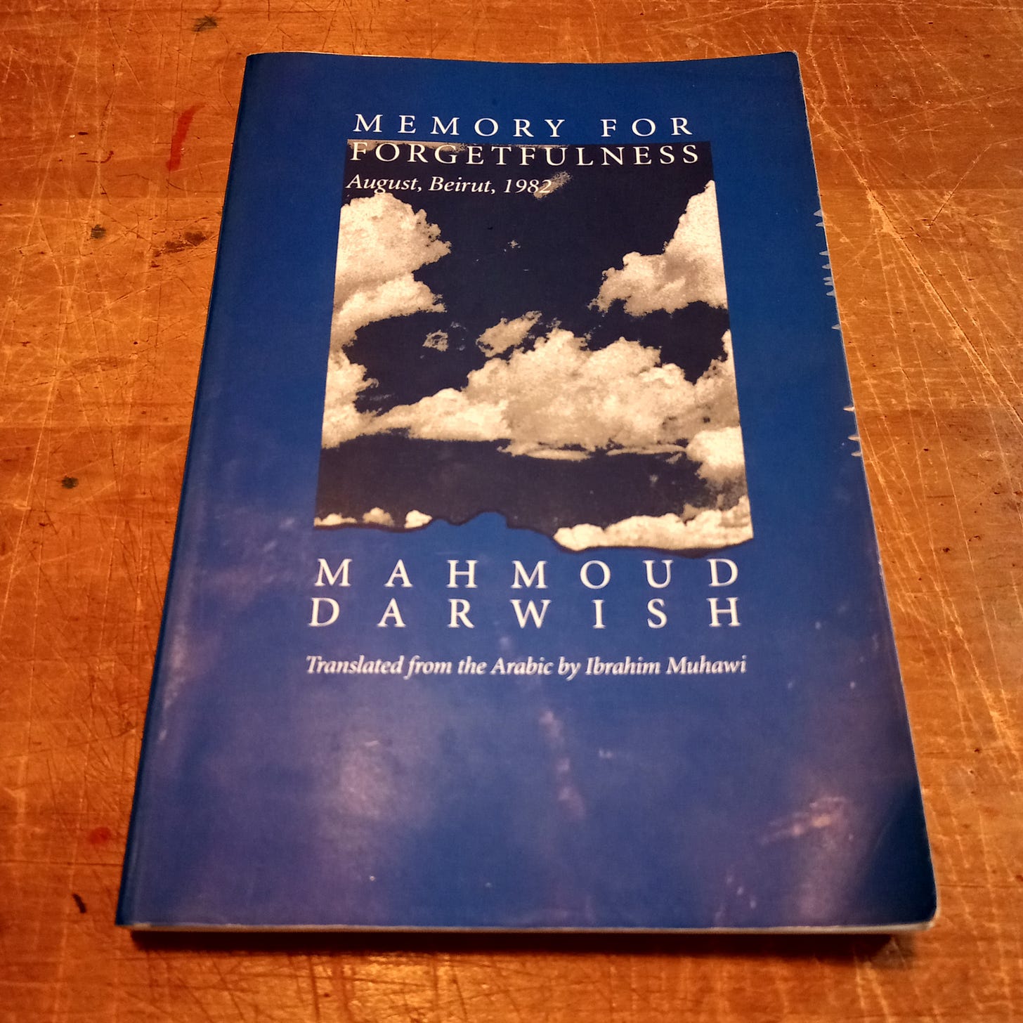 A copy of Mahmoud Darwish's Memory for Forgetfulness, with white clouds on a blue cover