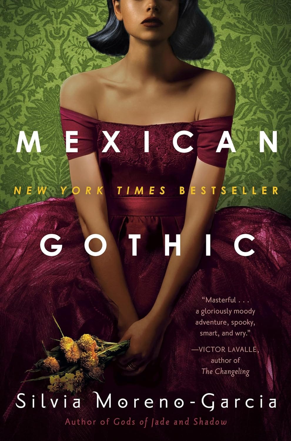 The cover of Mexican Gothic, a young woman in a burgundy dress holding yellow flowers in front of a green paisley background