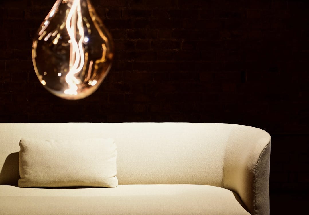 Free A contemporary interior featuring a glowing light bulb and a stylish beige sofa against a dark backdrop. Stock Photo