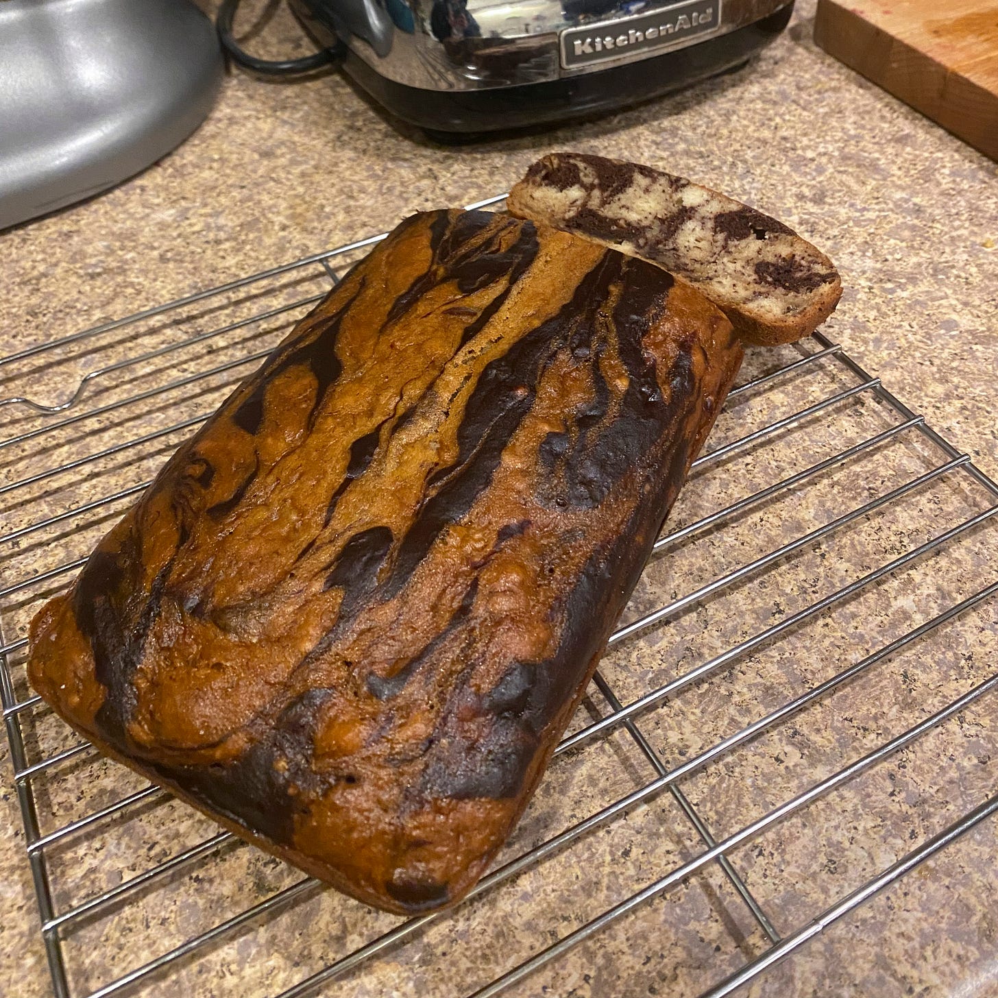 On a wire rack, a marbled loaf of banana bread with the end sliced off.