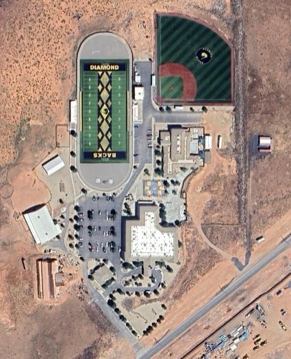 A satellite photograph of a group of buildings in the desert, with a full American football field and baseball diamond