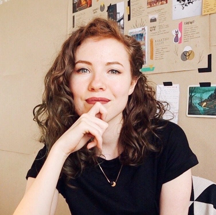 Rachael Stephen is a white woman with red wavy hair. She is wearing lipstick, a black tee shirt, and is smiling and looking at the camera.