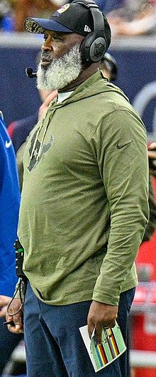 Photograph of Smith wearing a Texans sweatshirt, Texans baseball cap and headset on the Texans sideline