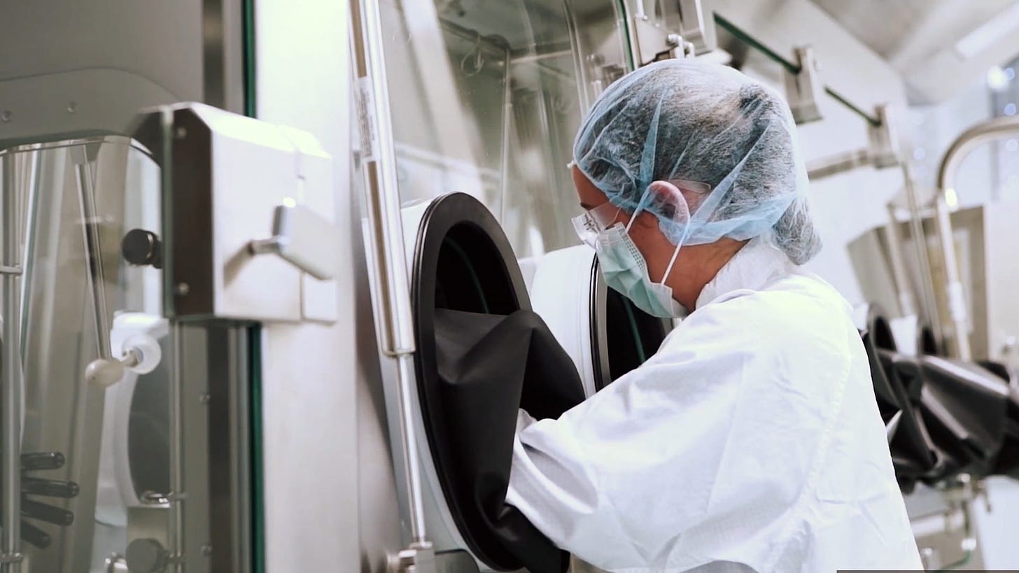 A lab employee in protective gear works on a section of the mRNA vaccine production line