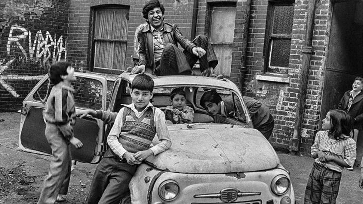 A black and white photograph of children playing in and on an abandoned car