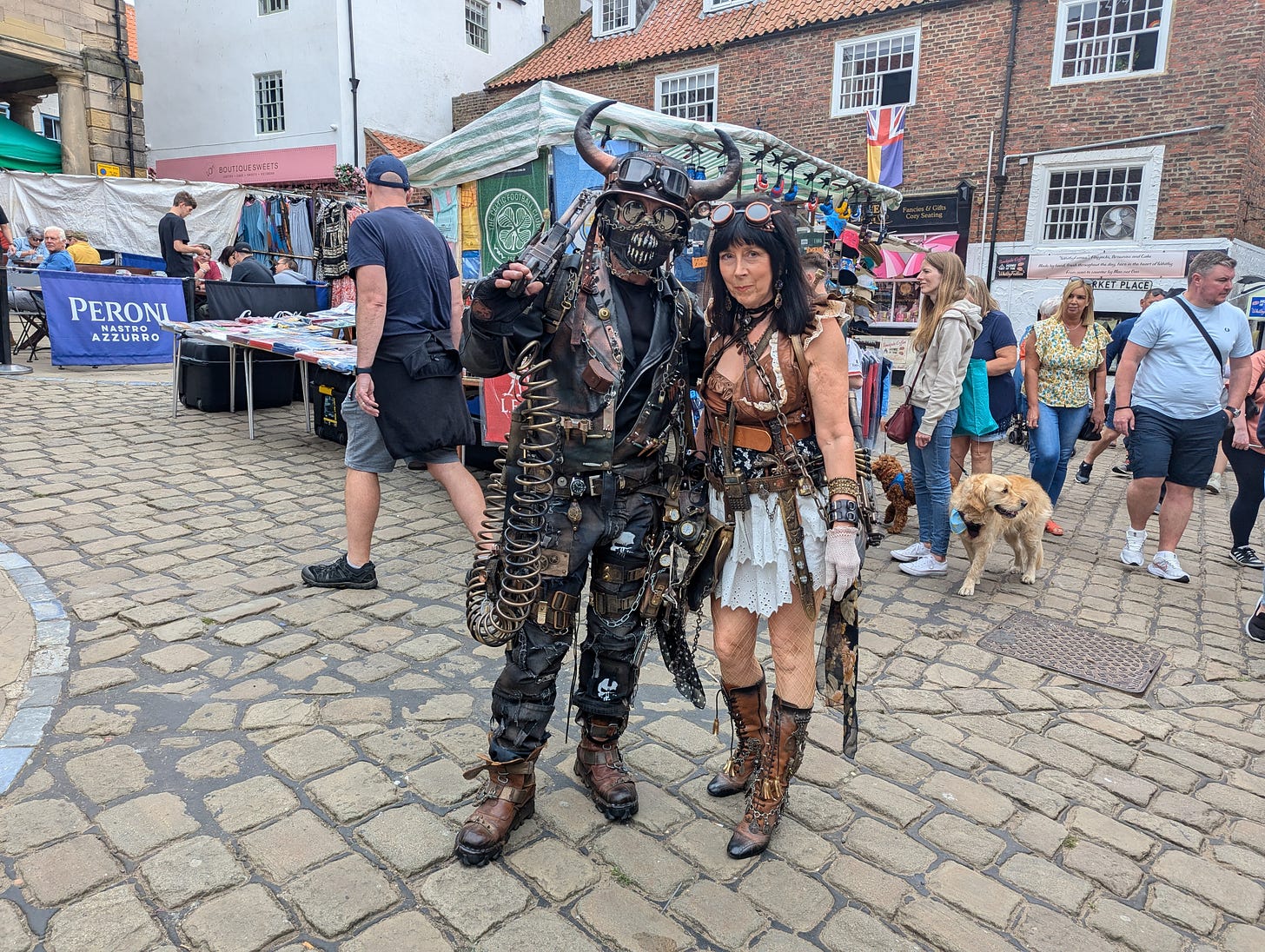 A steampunk couple pose for the camera in front of market stalls