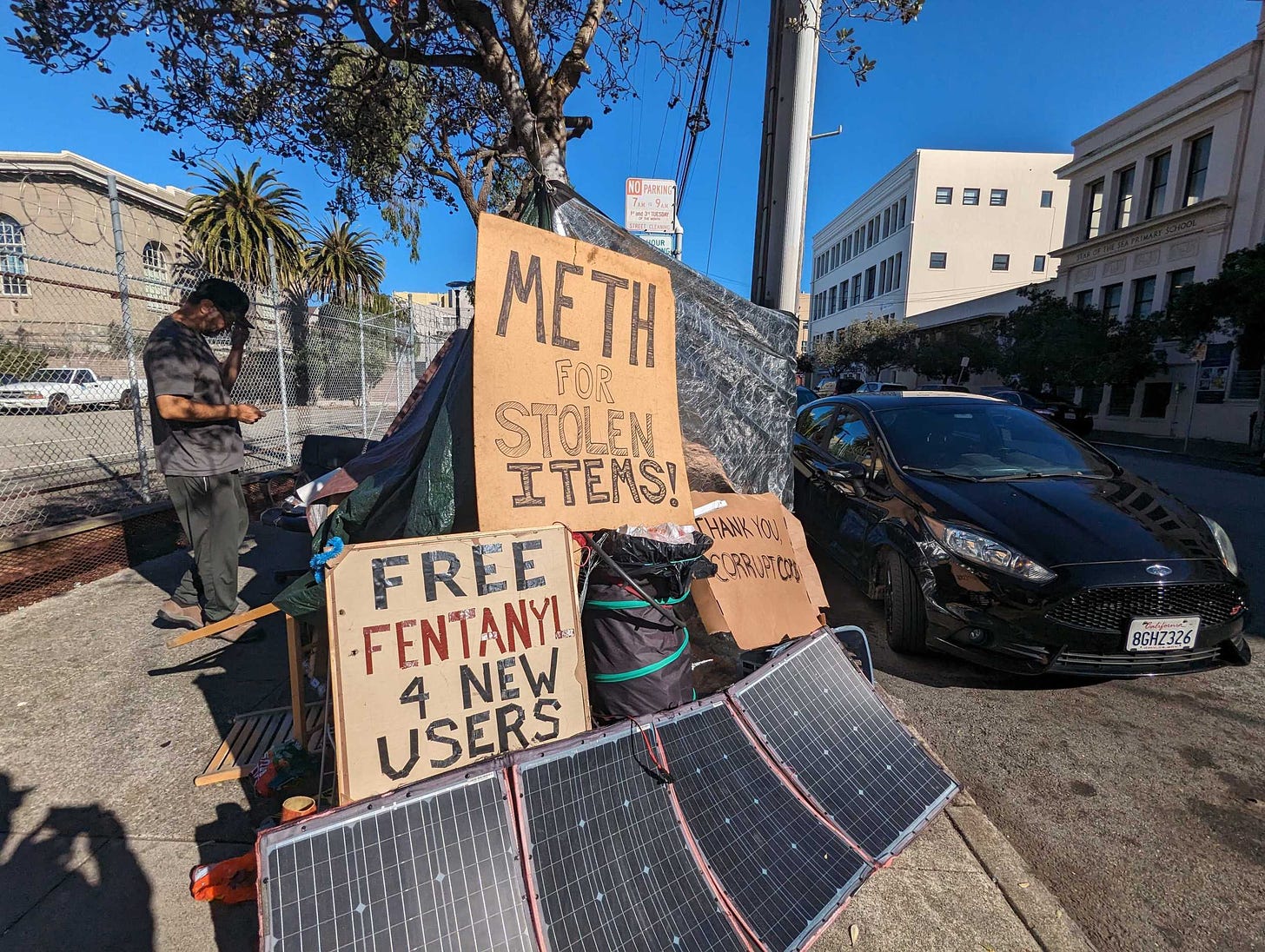 Signs reading "Meth for stolen items" and "free fentanyl 4 new users" sit atop Joseph Adam Moore's encampment on Ninth Avenue north of Geary Boulevard in San Francisco's Inner Richmond neighborhood.
