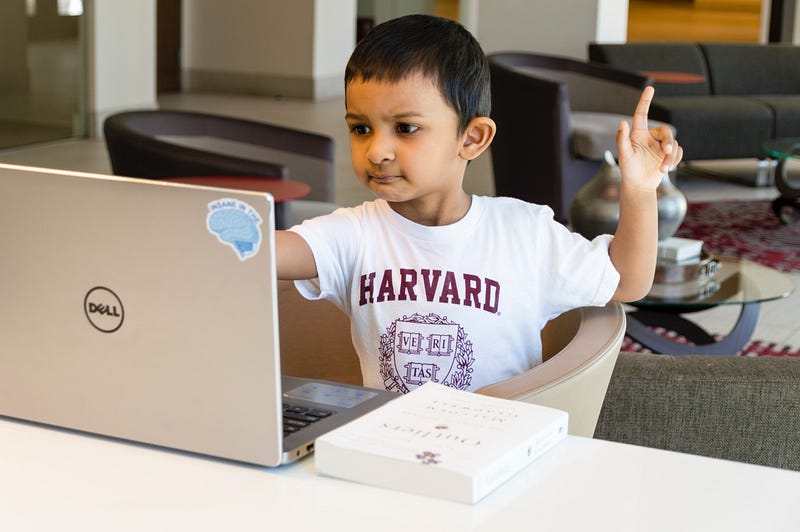 Young child with raised finger asking a question while looking at a laptop