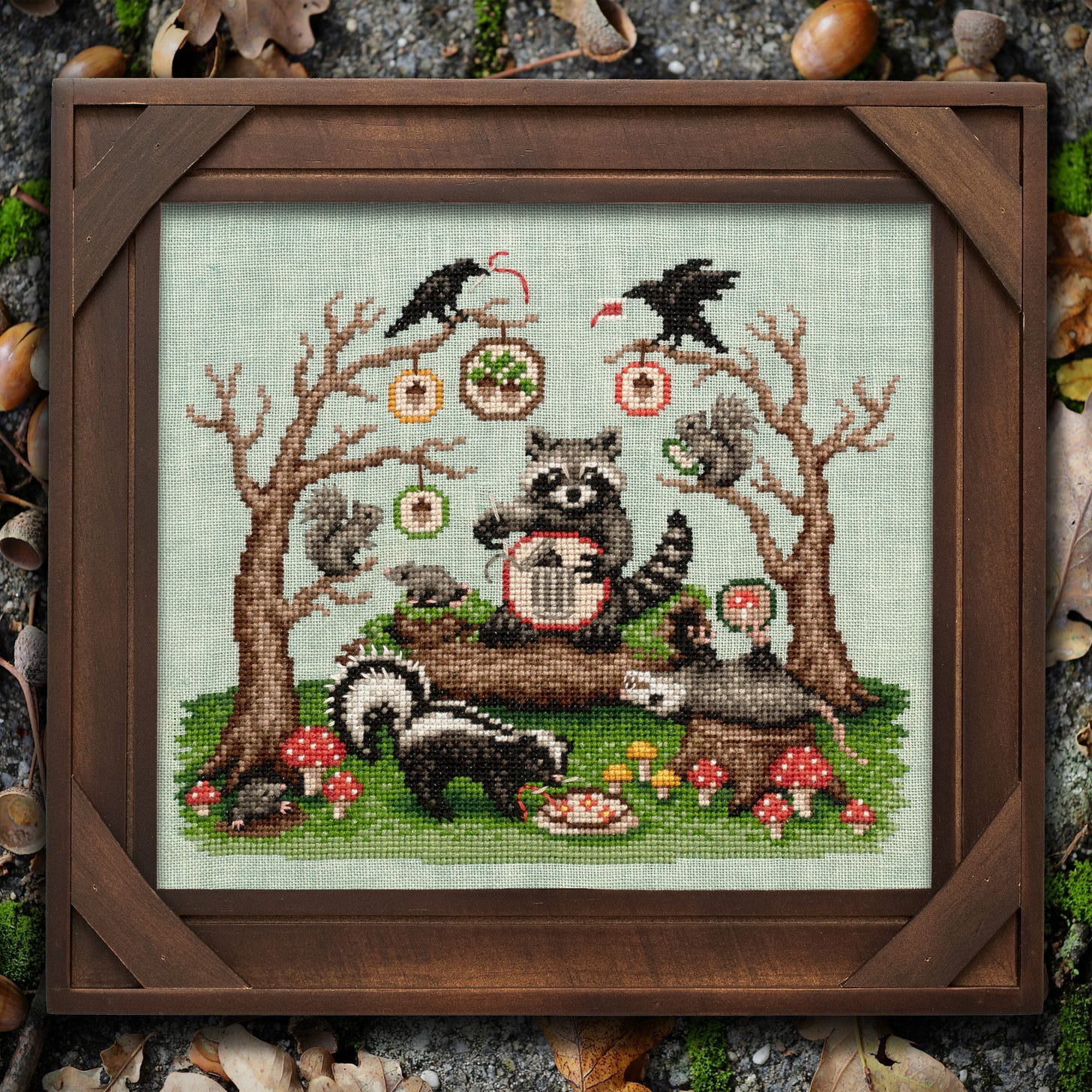 A cross stitch of a racoonn cross stitching, crows in trees, a possum playing dead, and lots of cross stitch elements like hoops and stitching.