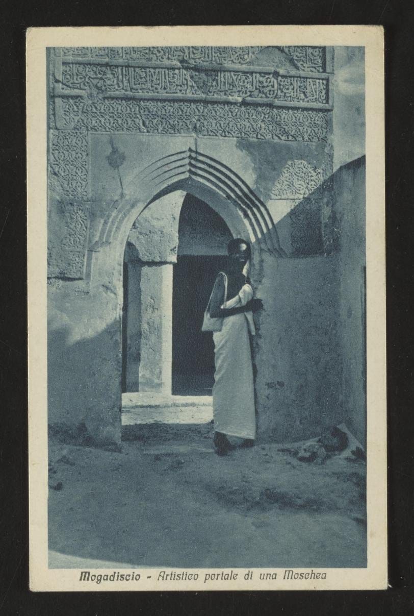 A person stands in the ornately carved doorway of a mosque in this black-and-white photo