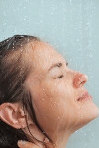 Powerful ways for a luxury shower routine-woman in shower with water splashing on face.