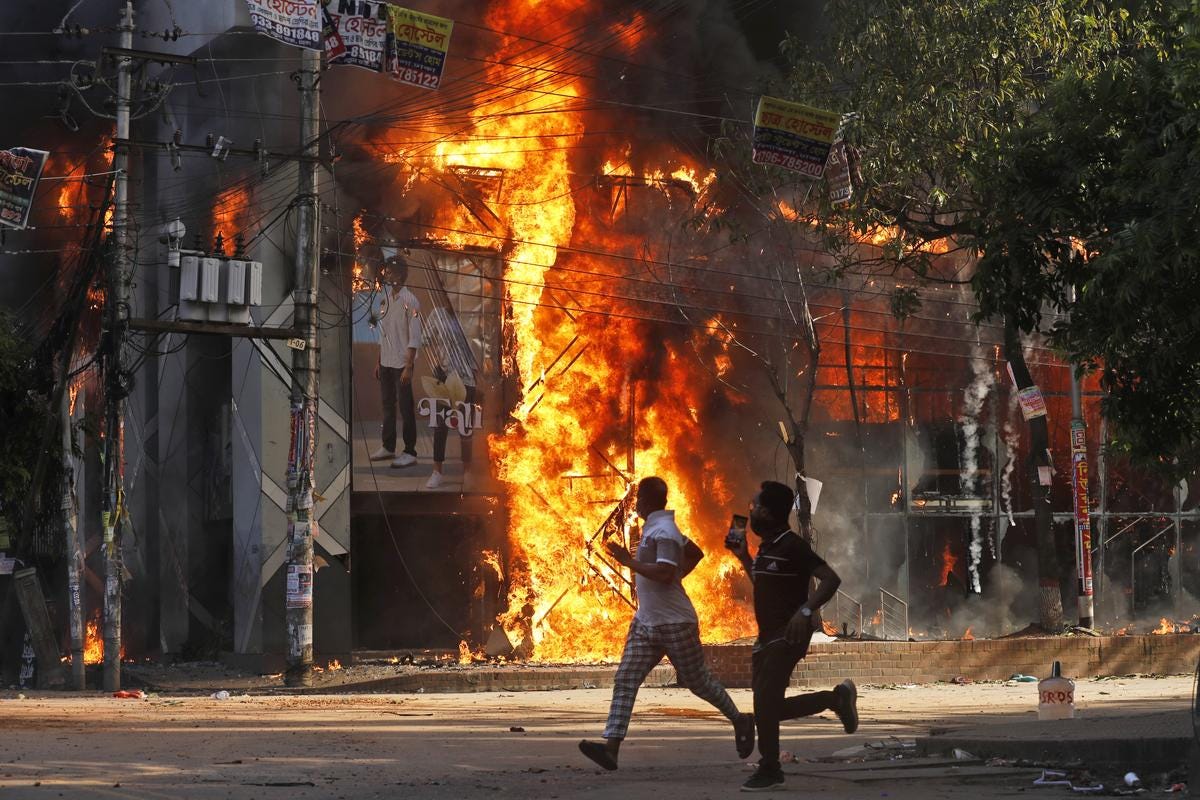 Men run past a shopping center which was set on fire by protesters during a rally against Prime Minister Sheikh Hasina and her government demanding justice for the victims killed in the recent countrywide deadly clashes, in Dhaka, Bangladesh, on August 4, 2024. 