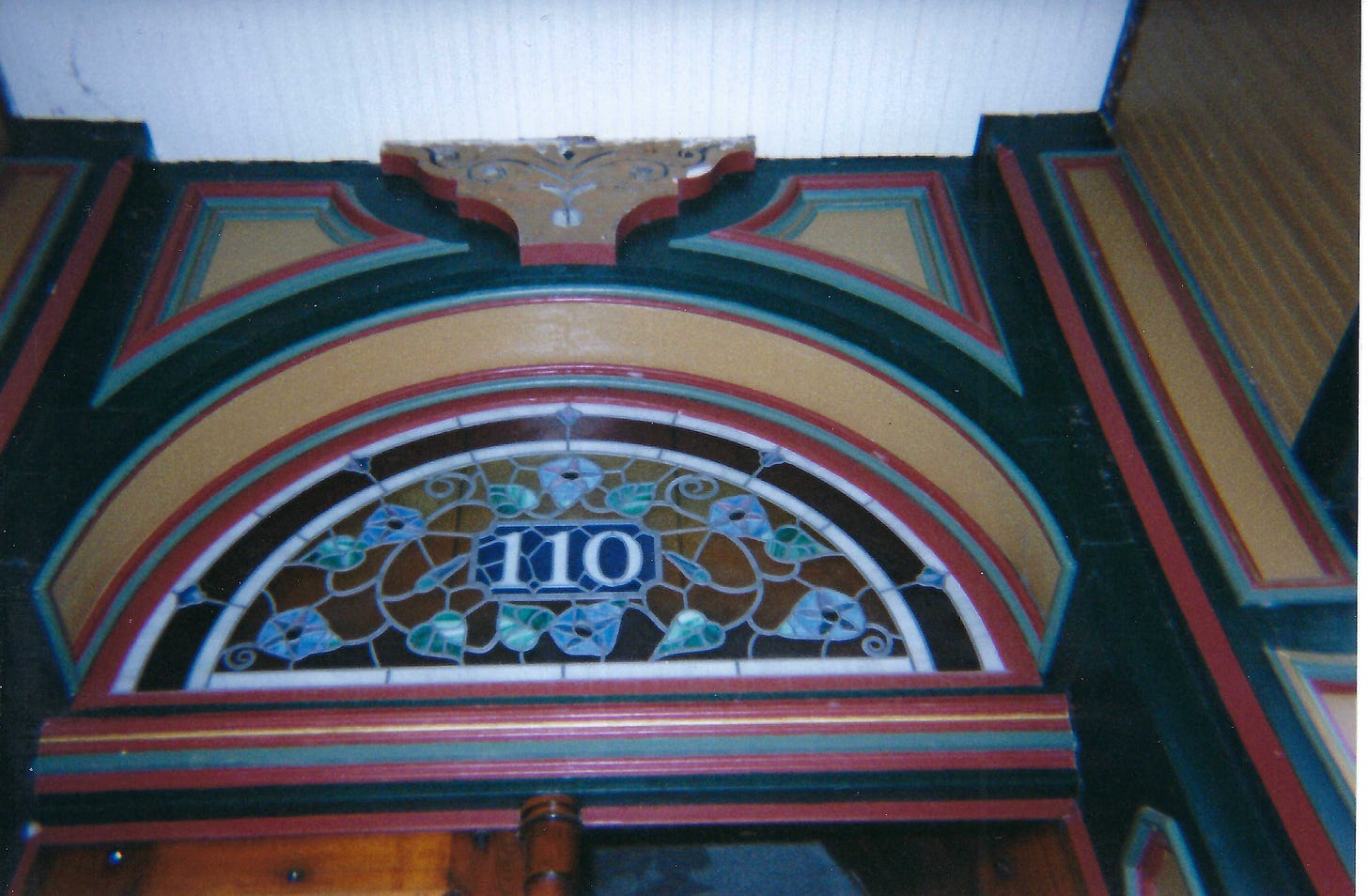 Crescent-shaped stained glass window. The window is amber, with the numbers 110 at the center. Blue flowers surround the numbers.