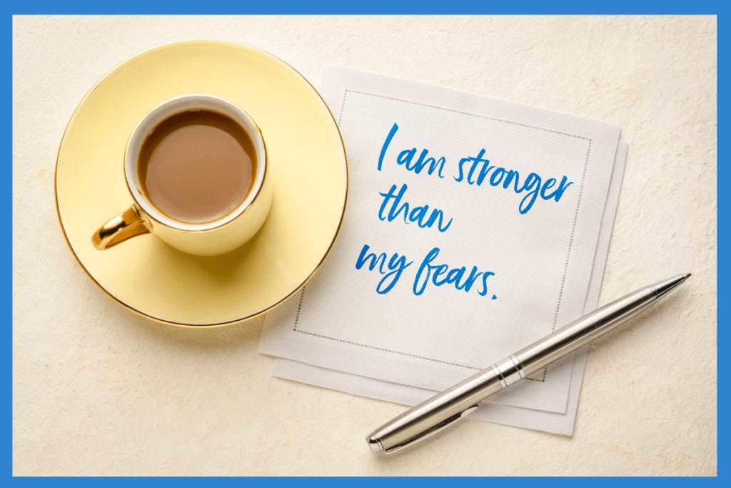 An affirmation for mindfulness, "I am stronger than my fears" written in blue ink on a napkin, next to a cup of coffee.
