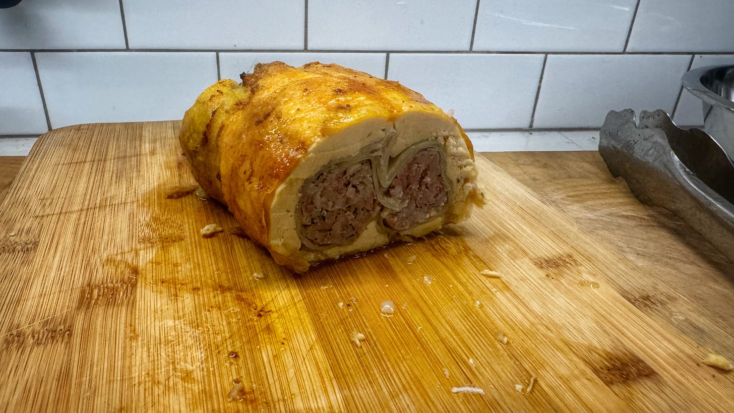 A chicken ballotine, stuffed with two cabbage rolls, cut in cross-section so the rolls are clearly visible, set on a cutting board.