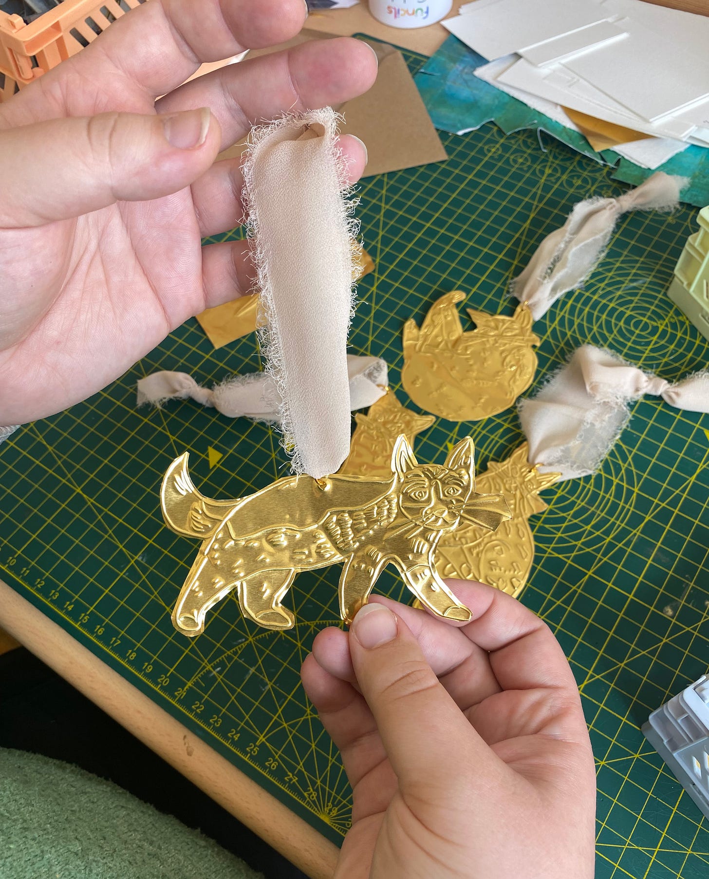 Two hands hold a brass tin embossed decoration of a cat.