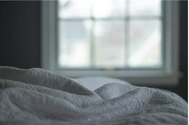 Image of white sheets ruffled on a bed with a window in the background.