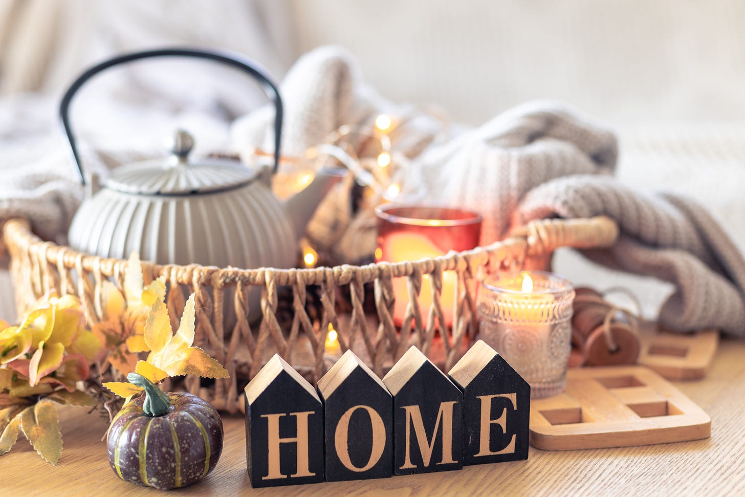 Tray over a table. It contains a round kettle, a candle and a sweater draped loosely over the side. In front of it there’s another candle, a little pumpkin and wooden blocks spelling “HOME”. 