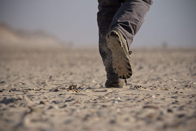 Close up of person's feet as they walk away on a dry, dusty surface.