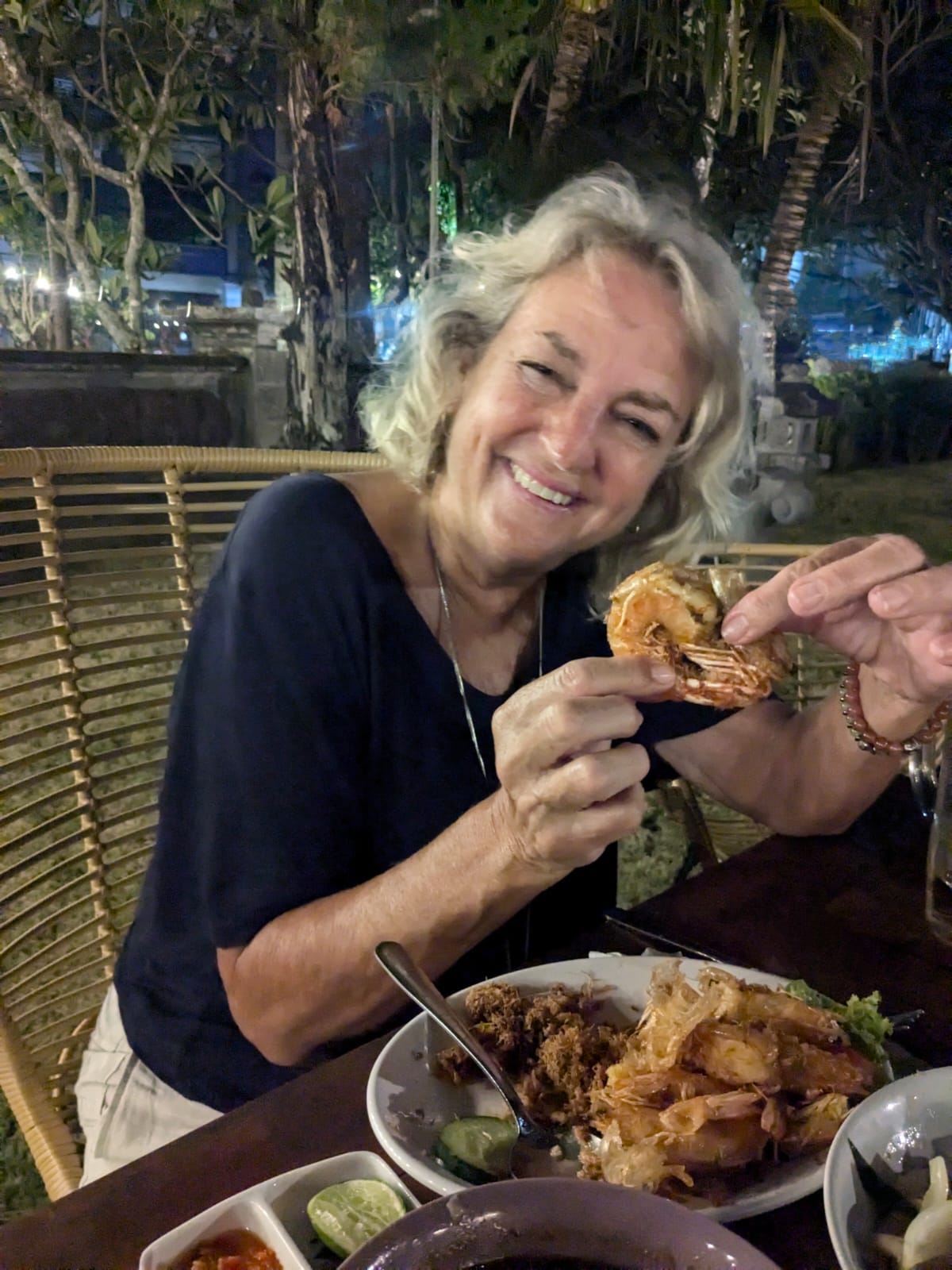 a middle aged woman smiling over an exotic looking dinner of shrimp