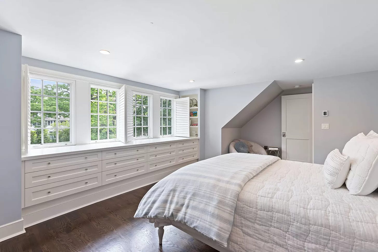 A modern-looking light gray bedroom with white cabinetry and a bed with white quilts.