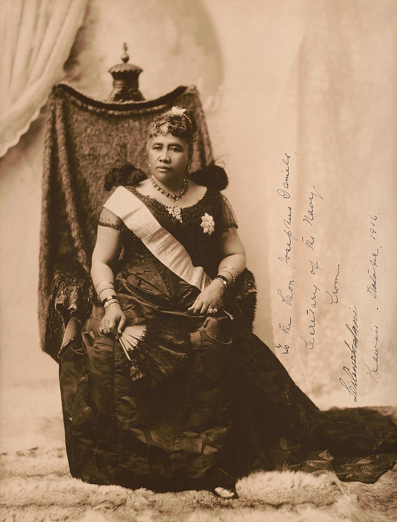 A sepia-tinted photograph of Queen Lili'uokalani. She sits on a throne holding a fan and wearing a dark gown. Her demeanor appears proud and determined. Text on photo reads: "To the Hon. Josephus Daniels, Secretary of the Navy, from Liliuokalani, Hawaii, October 1916."
