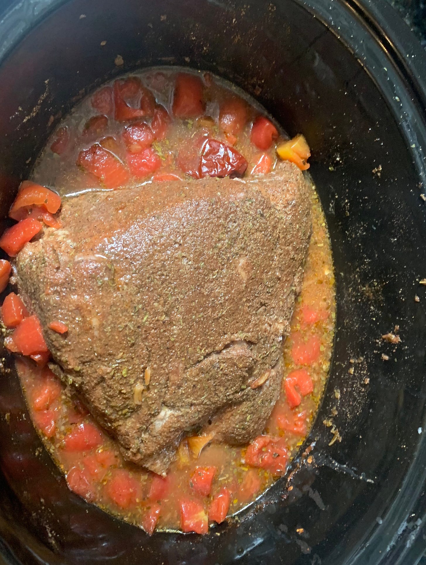 Pork shoulder in a slow cooker surrounded by tomatoes, chilis and liquid