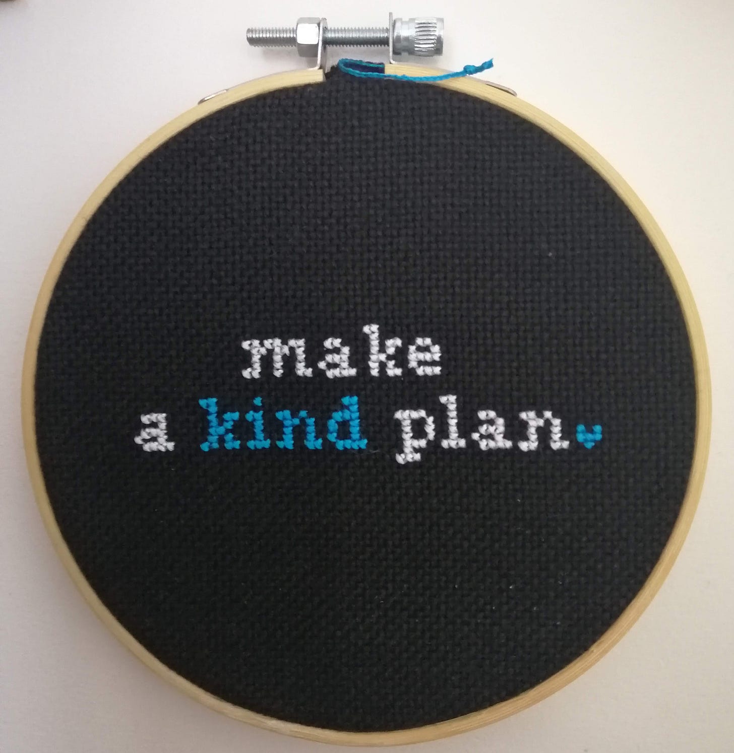 Cross stitch on black fabric framed in a hoop, the text reads "make a kind plan"