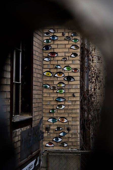 Image of a brink wall with pictures of different colour eyes pasted to the wall.