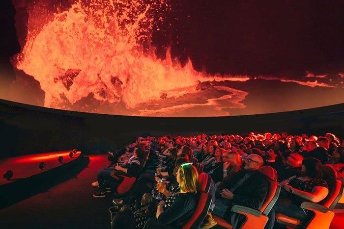 Image of a volcano erupting being viewed by lots of people in a planetarium