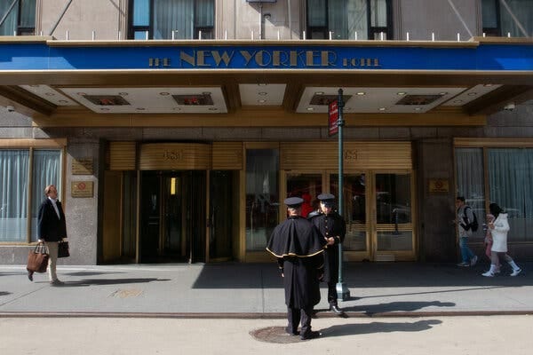 Doormen in uniform stand in the street in front of a marquee reading the New Yorker Hotel.