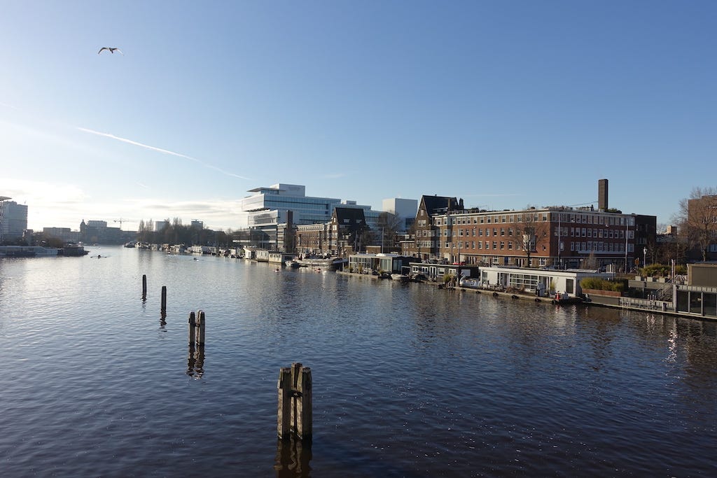 Looking out over the river Amstel from the middle of a bridge. The sky is blue with no clouds. 